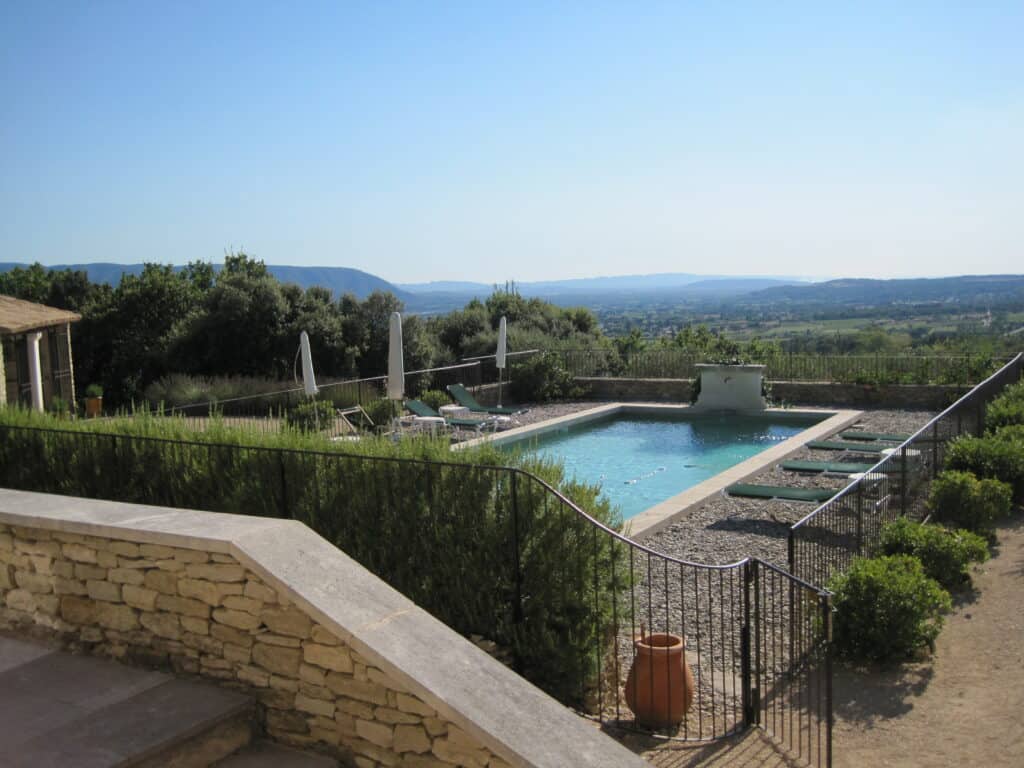 Swimming pool at villa in Provence enclosed by wrought iron fence and bushes with dark green deck chairs.