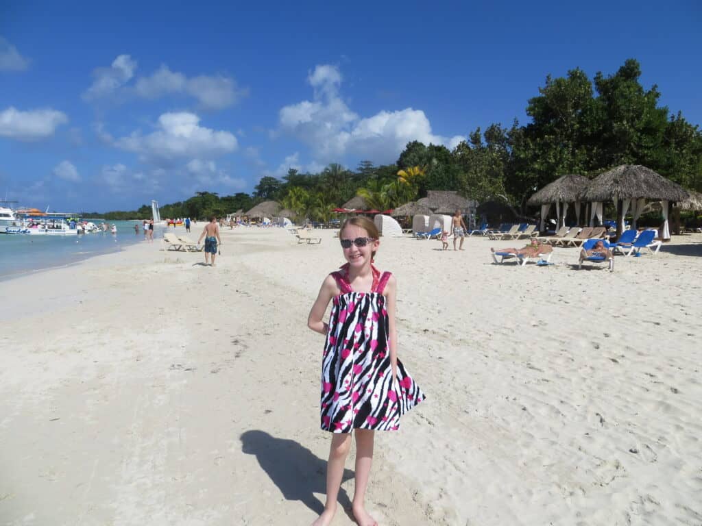 Young girl wearing black, white and pink cover-up and sunglasses standing on beach at Beaches Negril.