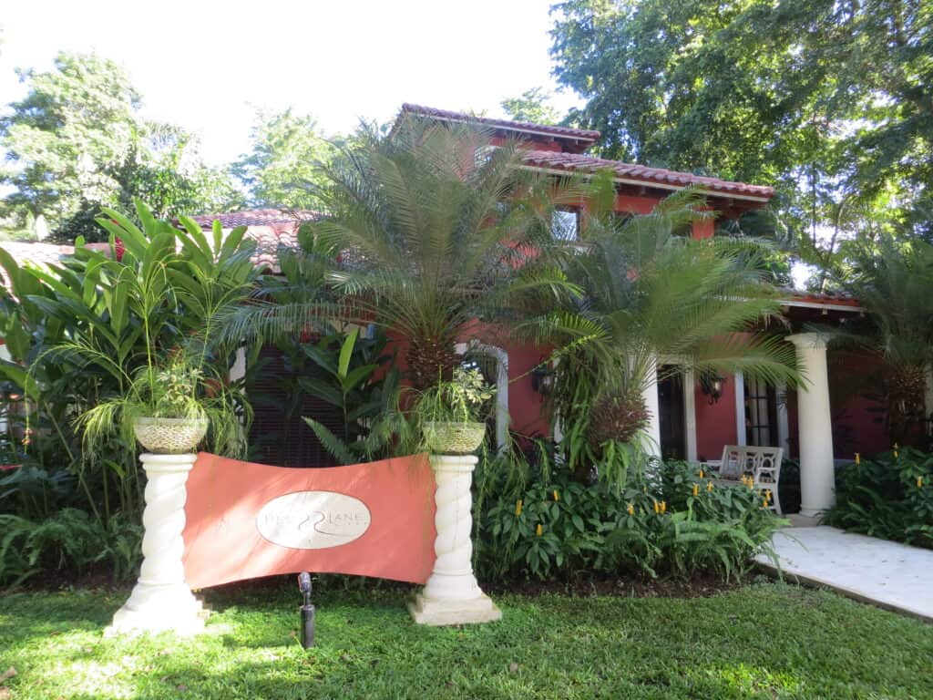 Exterior of spa at Beaches Negril - coral coloured building with white columns surrounded by lush green foliage.