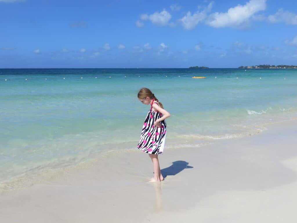 Young girl wearing black, white and pink cover-up walking on beach along the edge of the ocean at Beaches Negril, Jamaica.