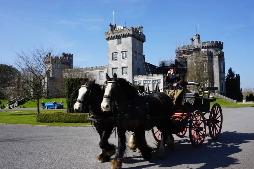 Two horses pulling cart with driver and Dromoland Castle in background.