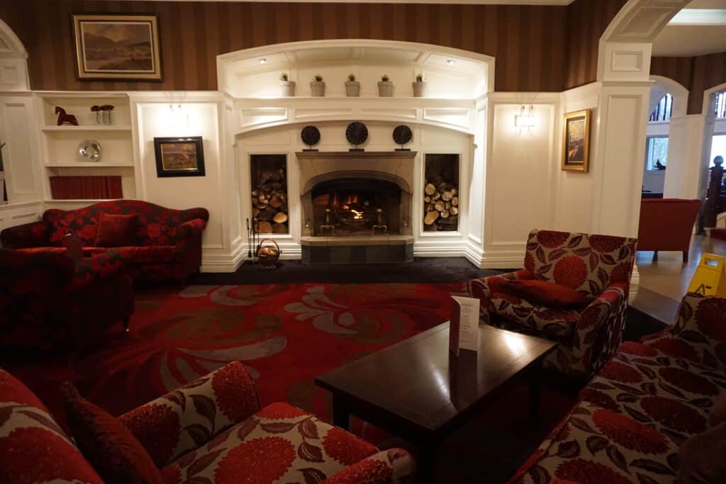 Lobby seating area at the Killarney Park Hotel - white woodwork around fireplace and shelves, dark burgundy carpet and burgundy and patterned chairs and sofa with dark wood table.