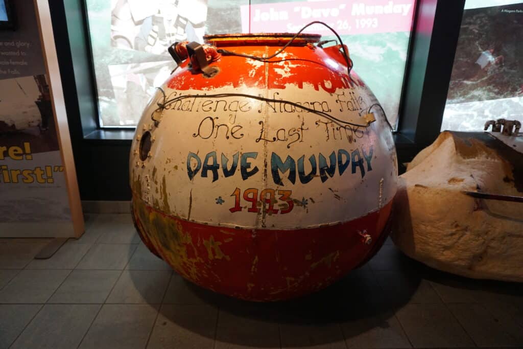 Banged up red and white circular "barrel" with words painted on it - Dave Munday 1993 - at Niagara Falls Daredevil Exhibit.