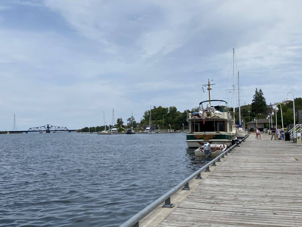 Boat docked along boardwalk in Little Current on Manitoulin Island with swing bridge in background.