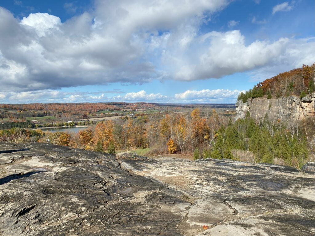 rocky escarpment with views of cliffs, reservoir and colourful fall trees stretching into the distance.