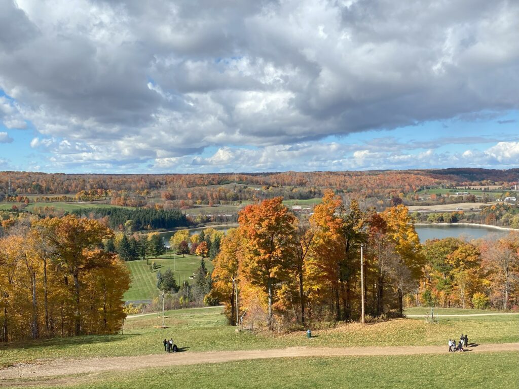 Kelso Conservation Area - two groups of people on trail at bottom of ski hill with colourful fall trees and reservoir in background.