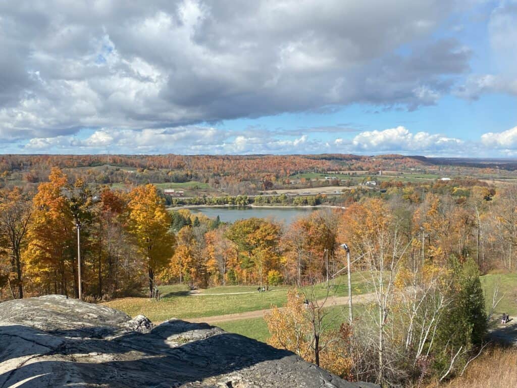 Standing on edge of rocky escarpment with views of the Kelso Reservoir surrounded by colourful fall trees.