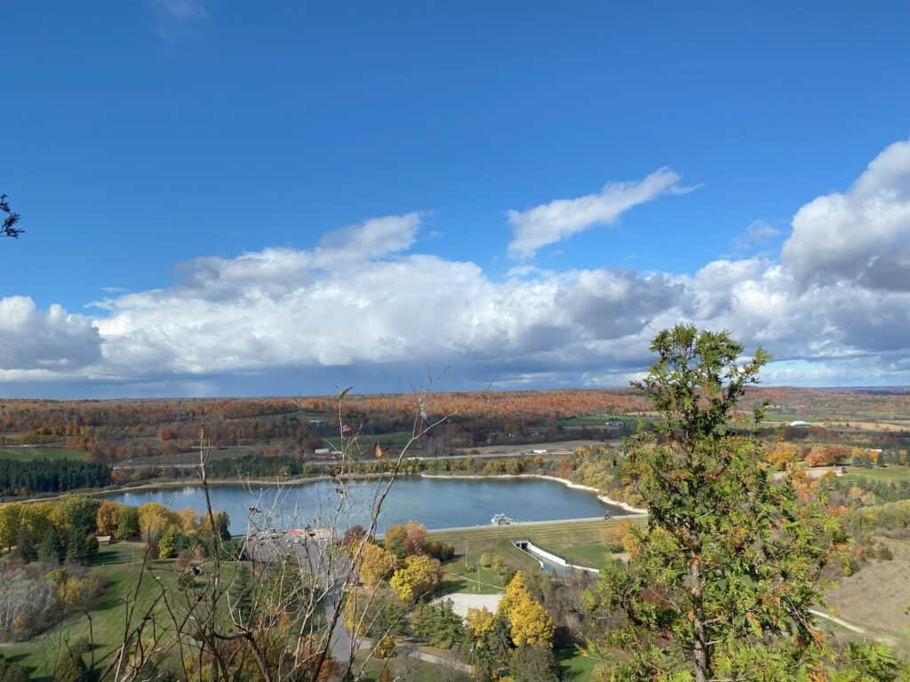 View of Kelso Reservoir from trail with colourful trees, bright blue sky and fluffy white clouds.