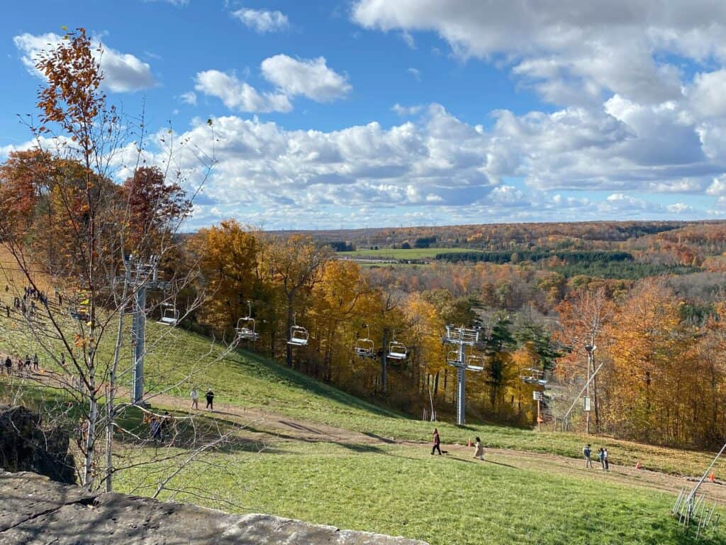 People walking uphill alongside chairlift with colourful fall trees in background at Kelso Conservation Area.