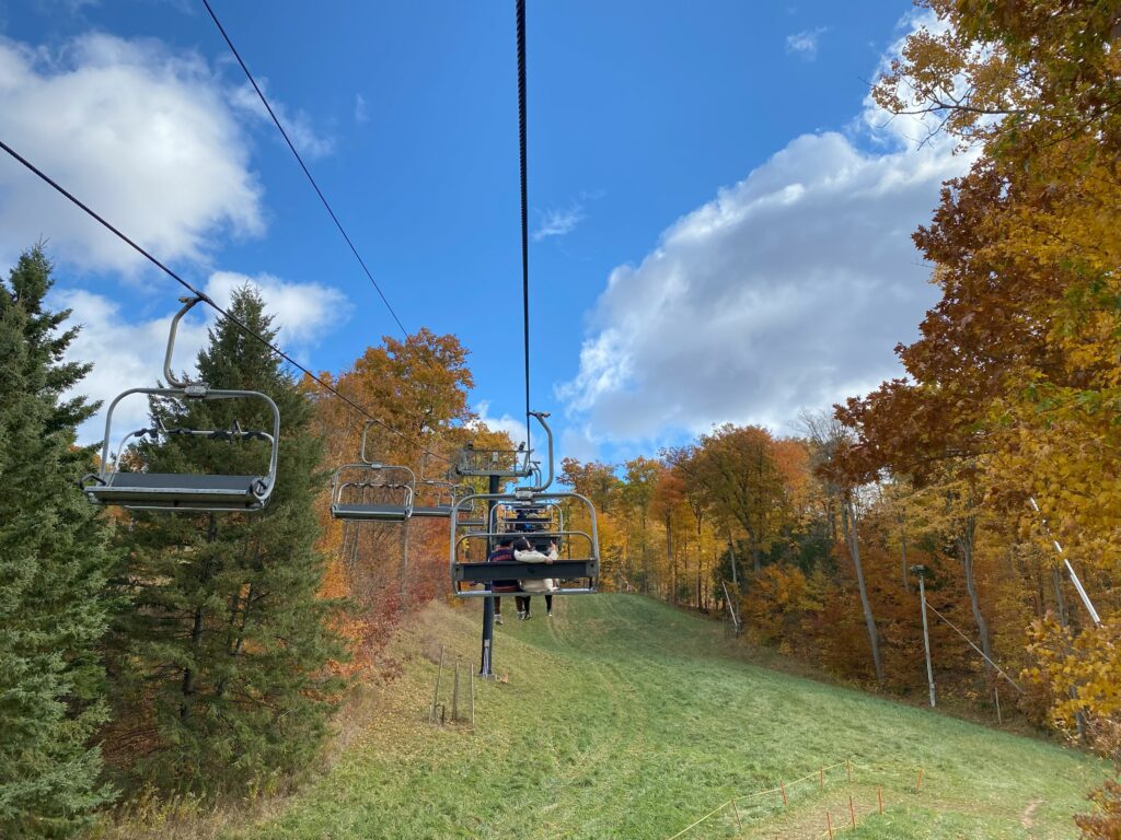 Kelso chairlift going uphill with colourful fall trees on either side.