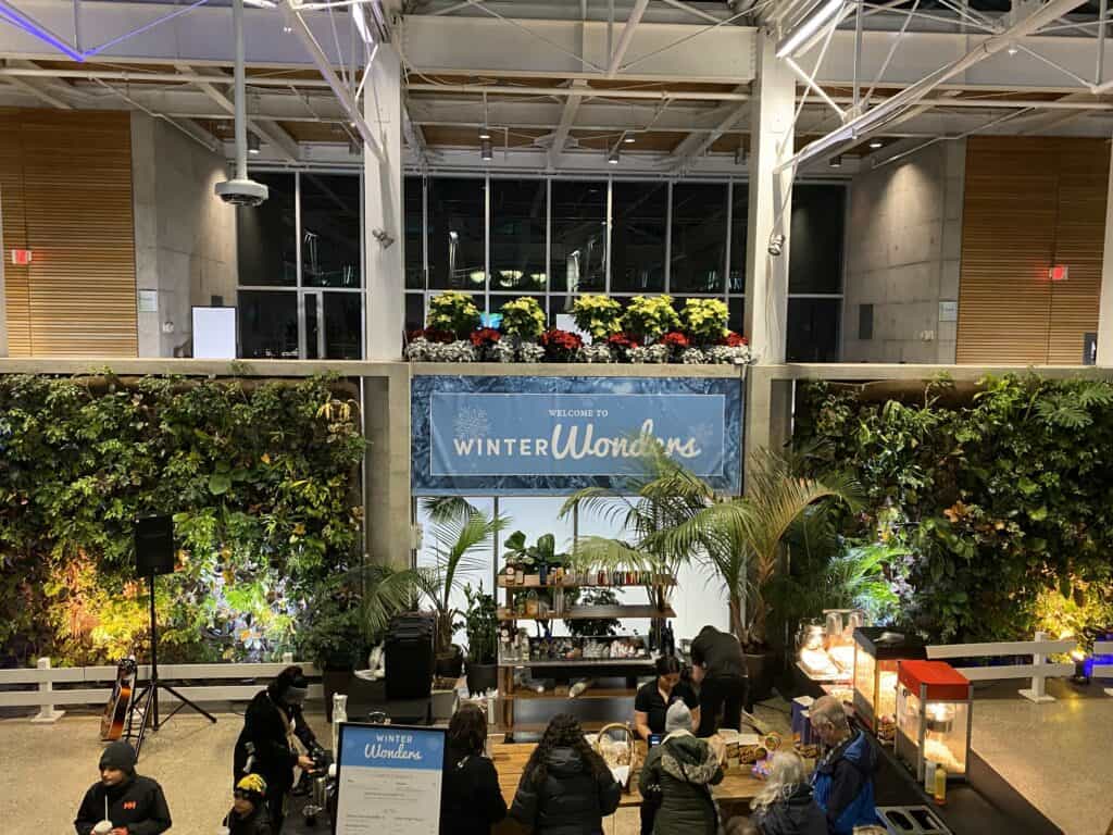 Visitors buying food and drinks in atrium of RBG with background of greenery and blue Welcome to Winter Wonders sign.