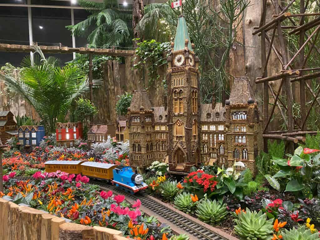 Thomas the Tank engine pulling two cars on tracks passing Canadian Parliament buildings - botanical train display at the Royal Botanical Gardens during Winter Wonders event.