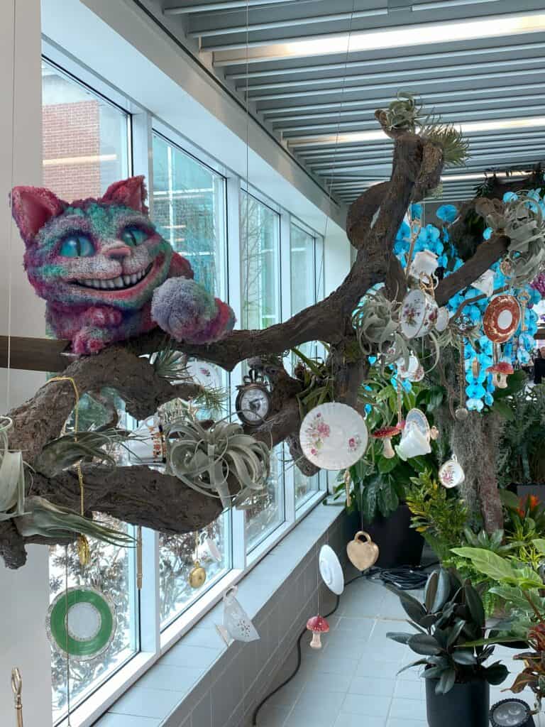 Cheshire Cat made from plant material on tree branch with hanging tea cups and saucers as well as flowers at the Royal Botanical Gardens' Alice in Bloomland showcase. 