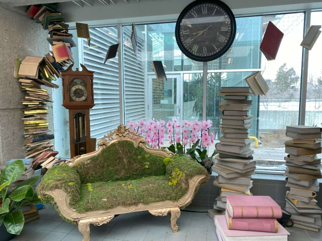 Royal Botanical Gardens Alice in Bloomland winter showcase - entranceway display of sofa made from plant materials, pink orchards, stacks of books, grandfather clock and wall clock.