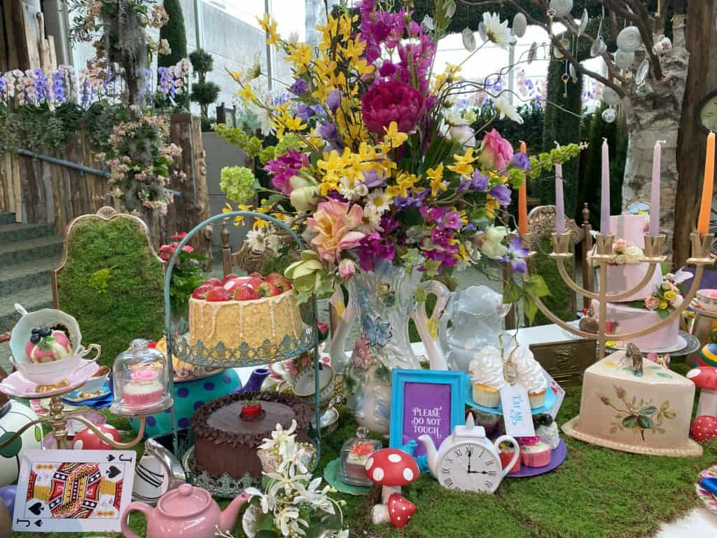 Brightly coloured floral centerpiece surrounded by whimsical tea items - Alice in Bloomland at Royal Botanical Gardens.